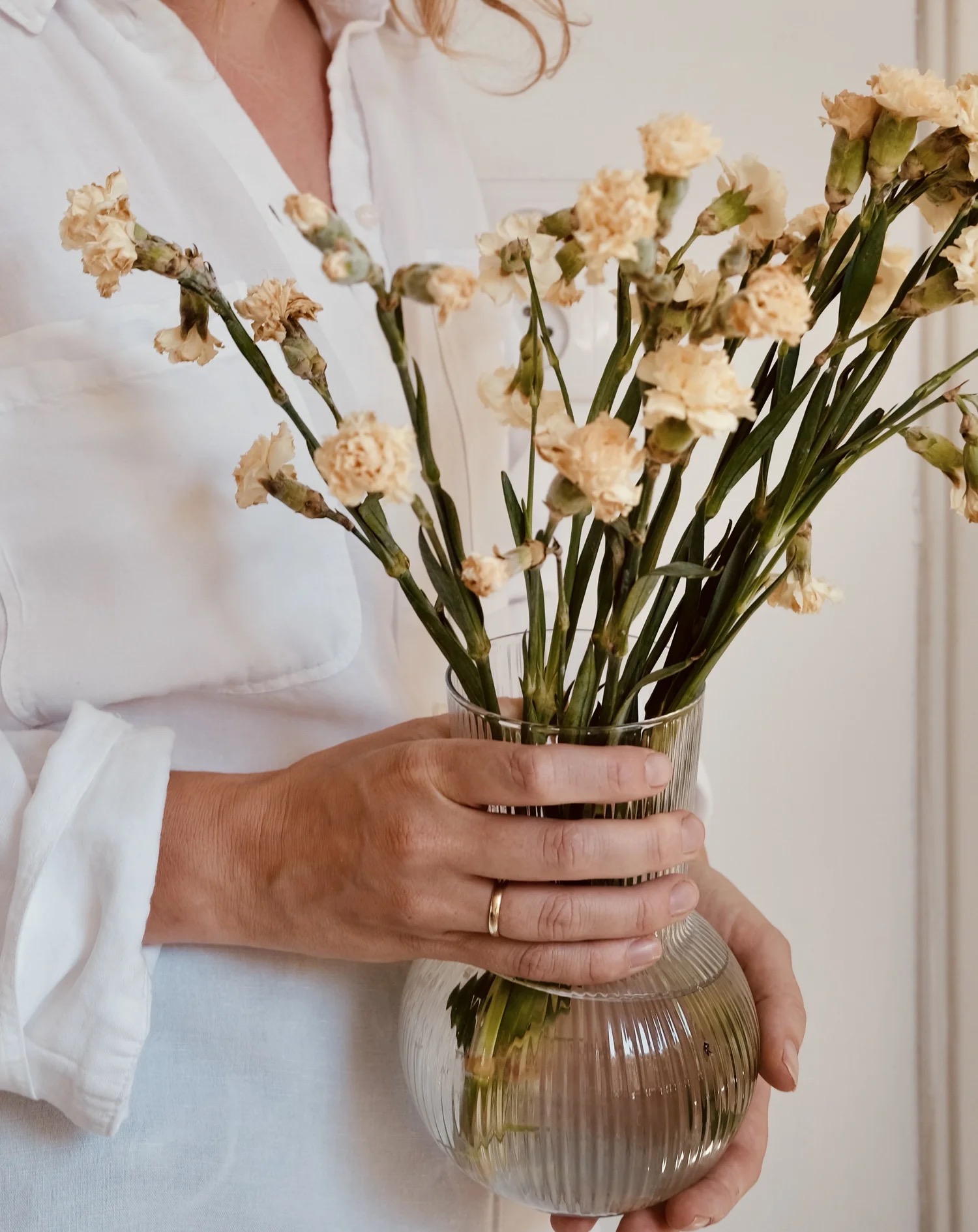 Handen die een glazen vaas met droogbloemen vasthouden